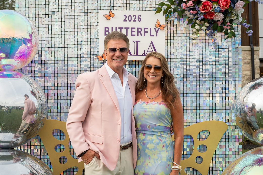 A couple posing in front of the 2026 Butterfly Gala sequin wall with mirrored balloons.