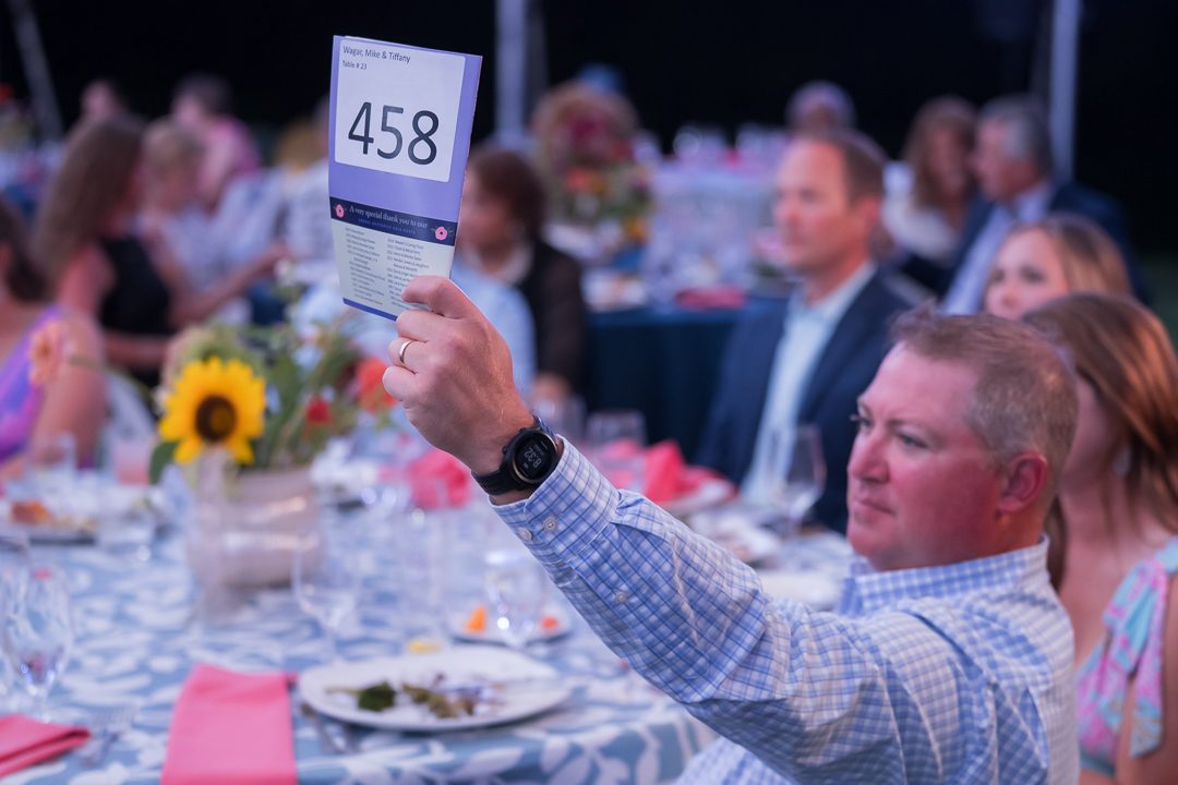A guest raising bidder paddle 458 at a gala dinner table.