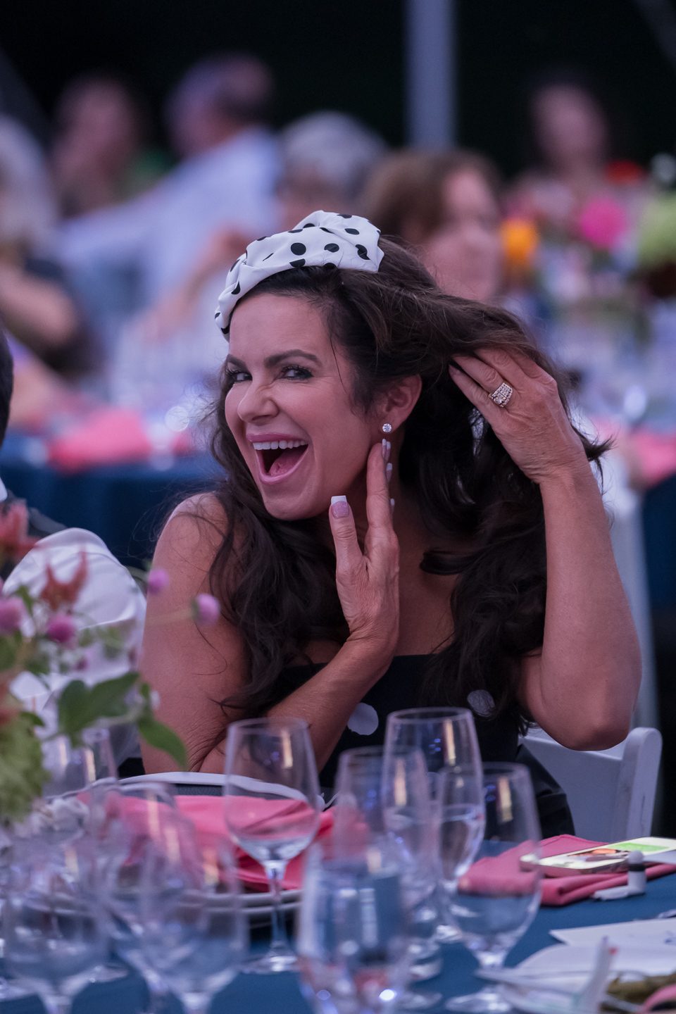 A woman in a polka-dot fascinator laughing at her table during the gala.