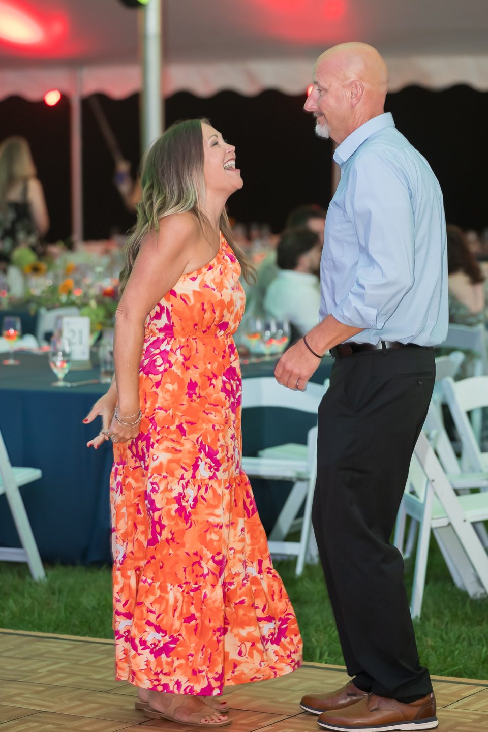 A couple dancing under the tent at the Butterfly Gala, she in an orange floral dress.